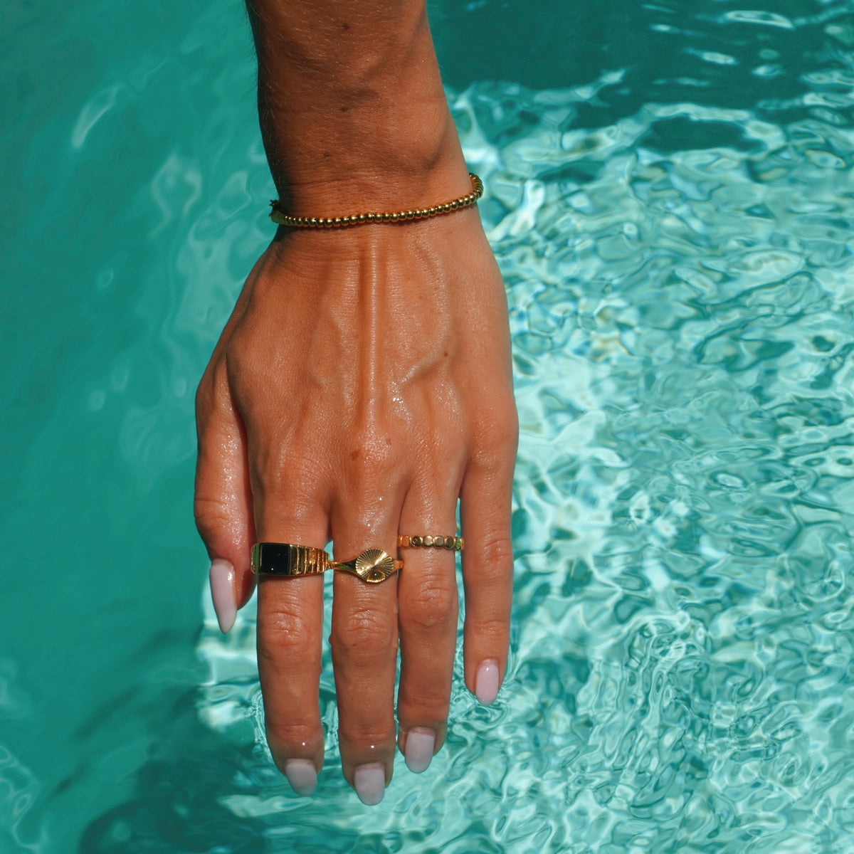 Gold sun signet ring and stacked gold rings worn in pool water